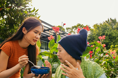 Daughter taking care health elderly mother who is sick with cancer sitting in wheelchair to eat soup to restore body and health but mother is bored of food doesn't want to eat blanの写真素材
