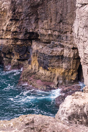 Vibrant turquoise ocean waves crash against the rocks on a sunny dayの写真素材