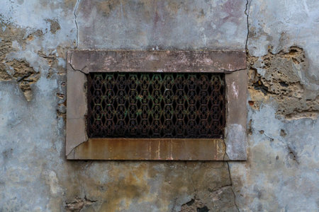Antique rusty metal grille on a small window in the wallの写真素材