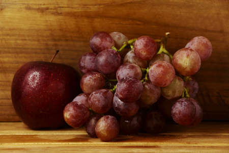 Red grapes and apple on a wooden floor.の写真素材