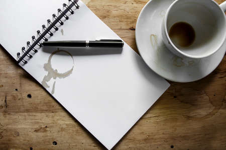 Coffee cup, spiral notebook and pen on the wooden table backgroundの写真素材
