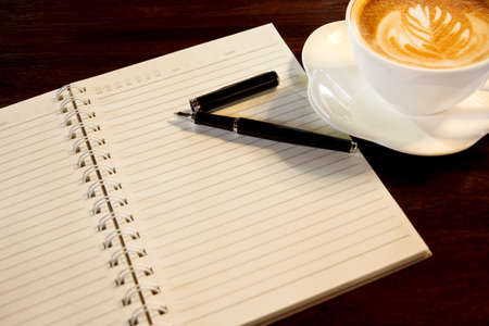 Coffee cup, spiral notebook and pen on the wooden table background