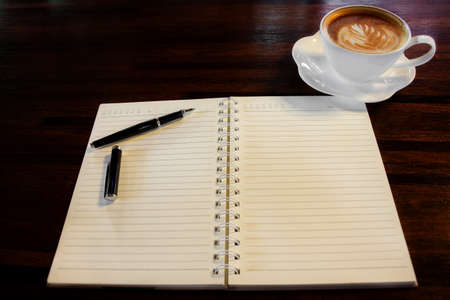 Coffee cup, spiral notebook and pen on the wooden table background