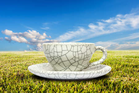 Cup of coffee on field of spring grass against blue sky with cloud.Shallow DOFの写真素材