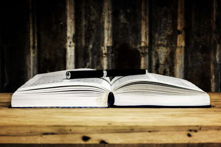 pen with open book on wood table against grunge backgroundの写真素材