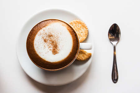 Cappuccino cup of coffee with cracker isolated on white background.