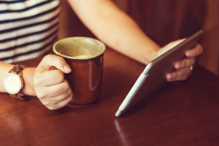 Asian woman using tablet computer in cafe drinking coffee. Focus on tablet. (Vintage process tone)の写真素材