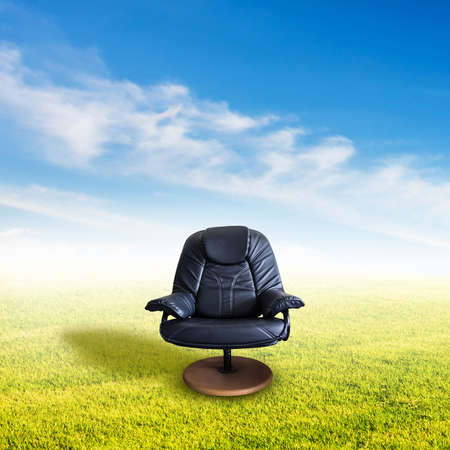 Black leather chair on grass field against sky and clouds. Natural office for relaxation.の写真素材