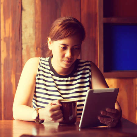 Asian woman using tablet computer in cafe drinking coffee. Focus on tablet. (Vintage process tone)