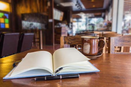Open notebook with coffee cup on table in cafe.の写真素材