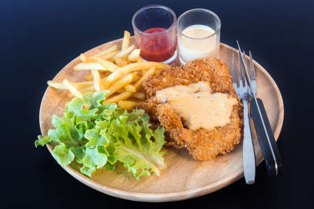 Fried fish steak with french fries in wooden plate on black tableの写真素材