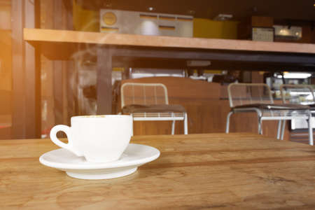 White cup of coffee with smoke on wooden table in cafe. warm tone.の写真素材