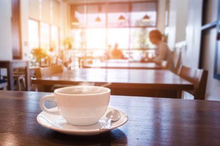 White cup of coffee with smoke on table in cafe. warm tone.の写真素材