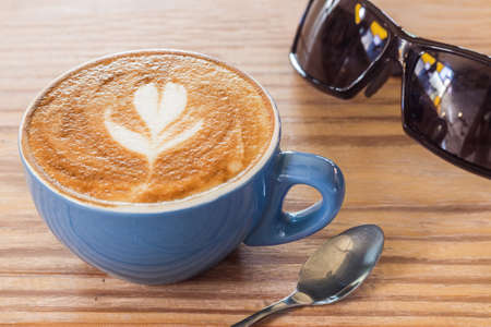 Close up coffee cup with steam and sunglasses on table in cafe. Selective focus.の写真素材