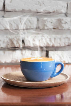 Hot Coffee cup with stream of vapour against white brick wall background.