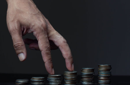 Coins stacked on each other in different positions, with a man's hand.の写真素材