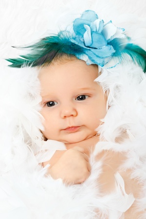 beautiful adorable baby with fashion flower in her hair, lying in fluffy feathersの写真素材