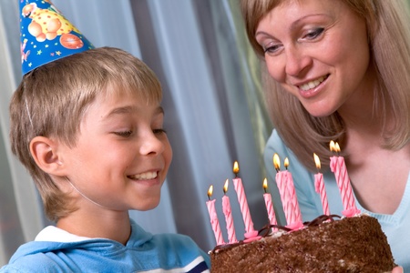 boy  with his mother blows out the candles on a birthday cakeの写真素材