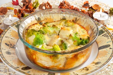 casserole with broccoli, chicken and cheese on plate, lighted candles on the tableの写真素材