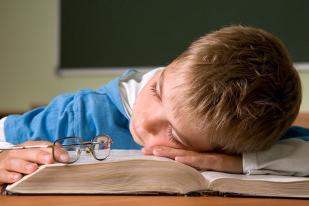 tired schoolboy sleep on a book in classroomの写真素材