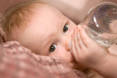 Baby boy drinking water herself from baby bottleの写真素材