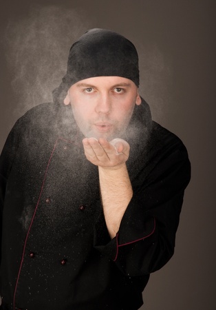 Chef in black uniform blows flour with the palmの写真素材