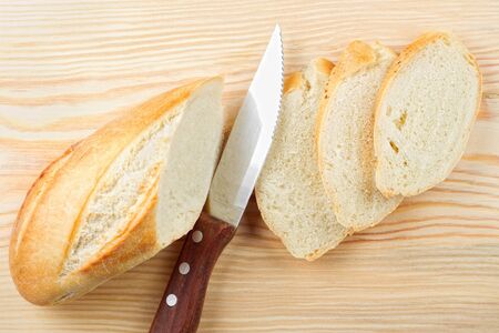 Freshly baked baguette sliced on wooden cutting board, knife, top view