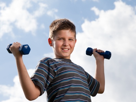 Happy boy lifting dumbbells outdoorsの写真素材