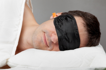Man with Sleeping mask and earplugs lying in bedの写真素材