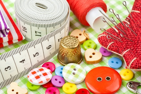 Sewing items: buttons, colorful fabrics, measuring tape, pin cushion, thimble, spool of thread  の写真素材