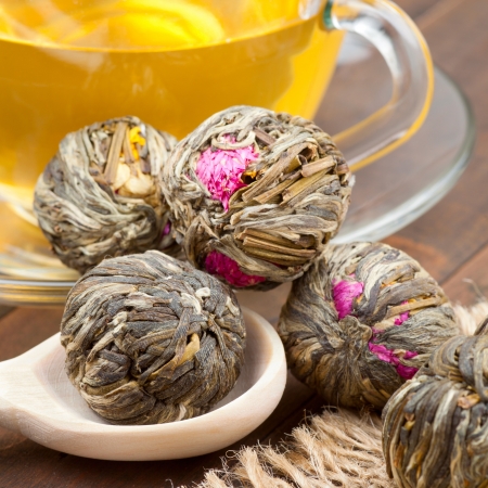 Green tea balls with flowers, tea cup and wooden spoon on kitchen tableの写真素材
