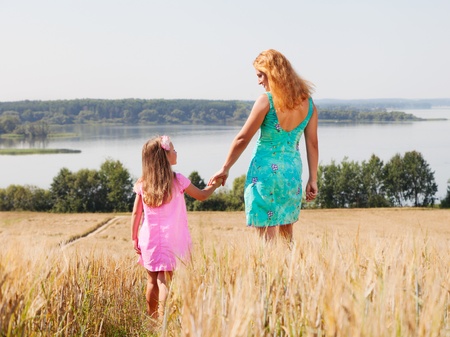 Mother and daughter walking  in summer field near lake on a sunny dayの写真素材
