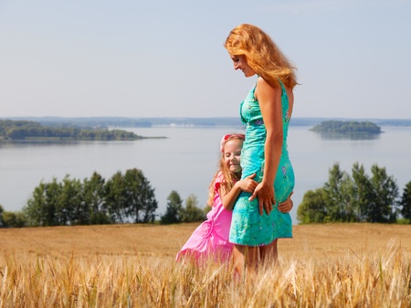 little girl hugging her mother in a wheat field near lake on a sunny dayの写真素材