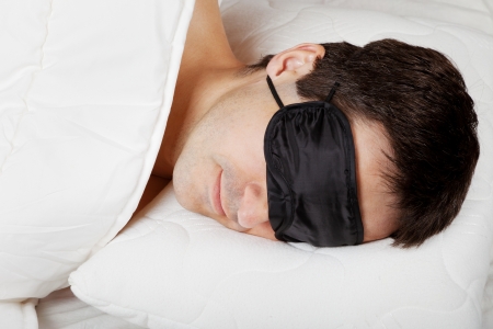 Man with Sleeping mask sleep lying in bedの写真素材