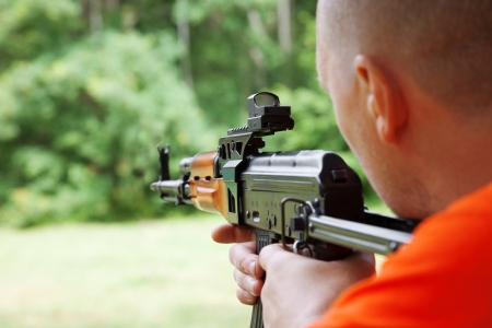 Man aiming at a target and shooting an automatic rifle for strikeball. Focus on the rifle sights.の写真素材