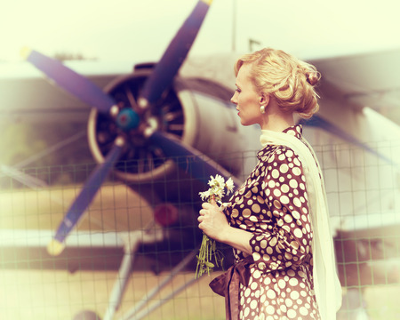 Vintage stylized photo of beautiful girl with a bouquet of daisies and plane on backgroundの写真素材