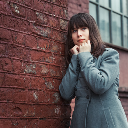 pensive beautiful young girl standing near a brick wall の写真素材