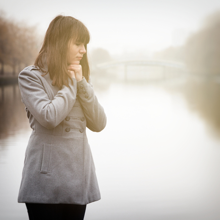 young pretty sad girl in cold weather near river in a fogの写真素材