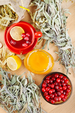 red cranberries, jar with honey, fruit tea cup, healing herbs and lemon on table, top viewの写真素材