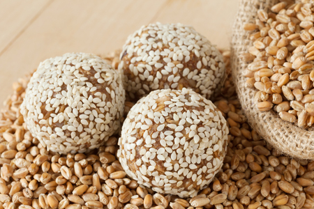 sweet balls from ground wheat sprouts with sesame seeds, grains in sack on wooden kitchen tableの写真素材
