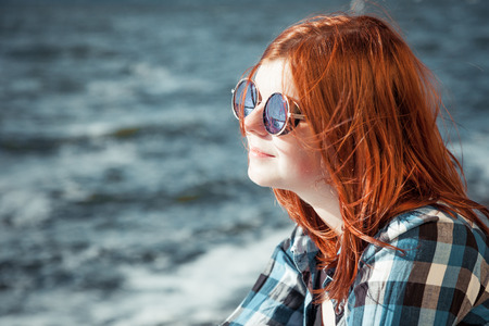 carefree beautiful red hair young woman in sunglasses over seascape
