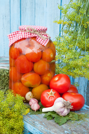 Homemade pickled tomatoes in glass jar. Fresh vegetables, dill and garlic on wooden boardの写真素材