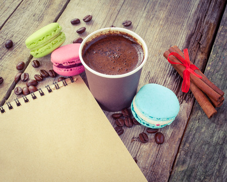 macaroons, espresso coffee cup, cinnamon sticks and sketch book on wooden rustic table, vintage stylized photoの写真素材