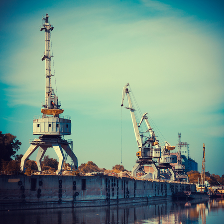Working cranes for cargo at the shipyard docks in river port, vintage stylized.の写真素材