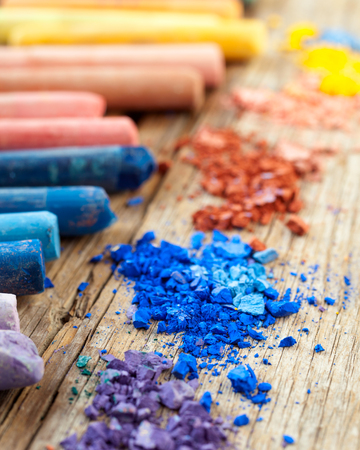 Collection of rainbow colored pastel crayons with crushed chalk on old wooden desk.の写真素材