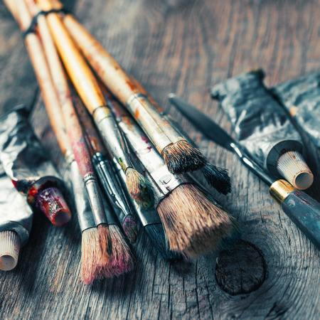 Artistic paintbrushes, tubes of oil paint, palette knife on old wooden desk. Vintage stylized.の写真素材