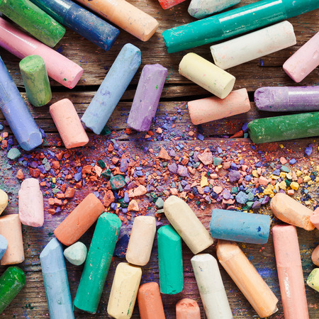 Collection of rainbow colored artistic pastel crayons with pigment dust on old wooden desk.の写真素材