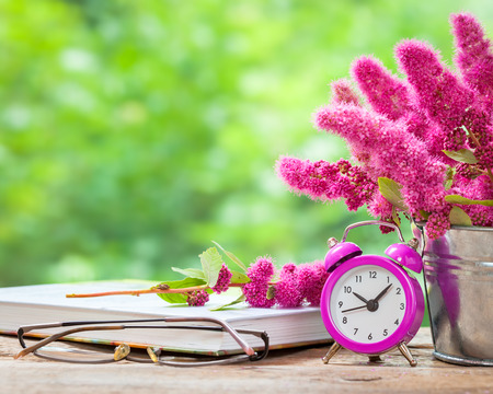 Vintage still life: flowers in bucket, pink alarm clock and bucket on wooden table outdoorsの写真素材
