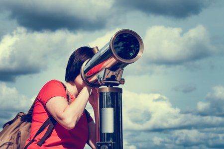 Young woman looking through tourist telescope, exploring landscape.の写真素材