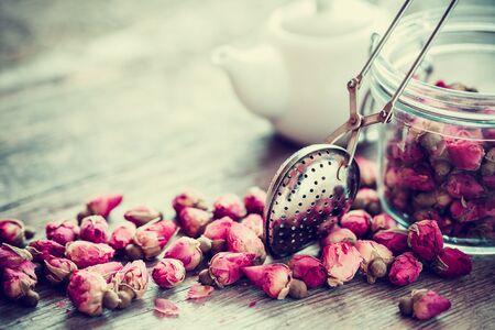 Rose buds tea, tea strainer closeup, glass jar and teapot on background. Selective focus.の写真素材